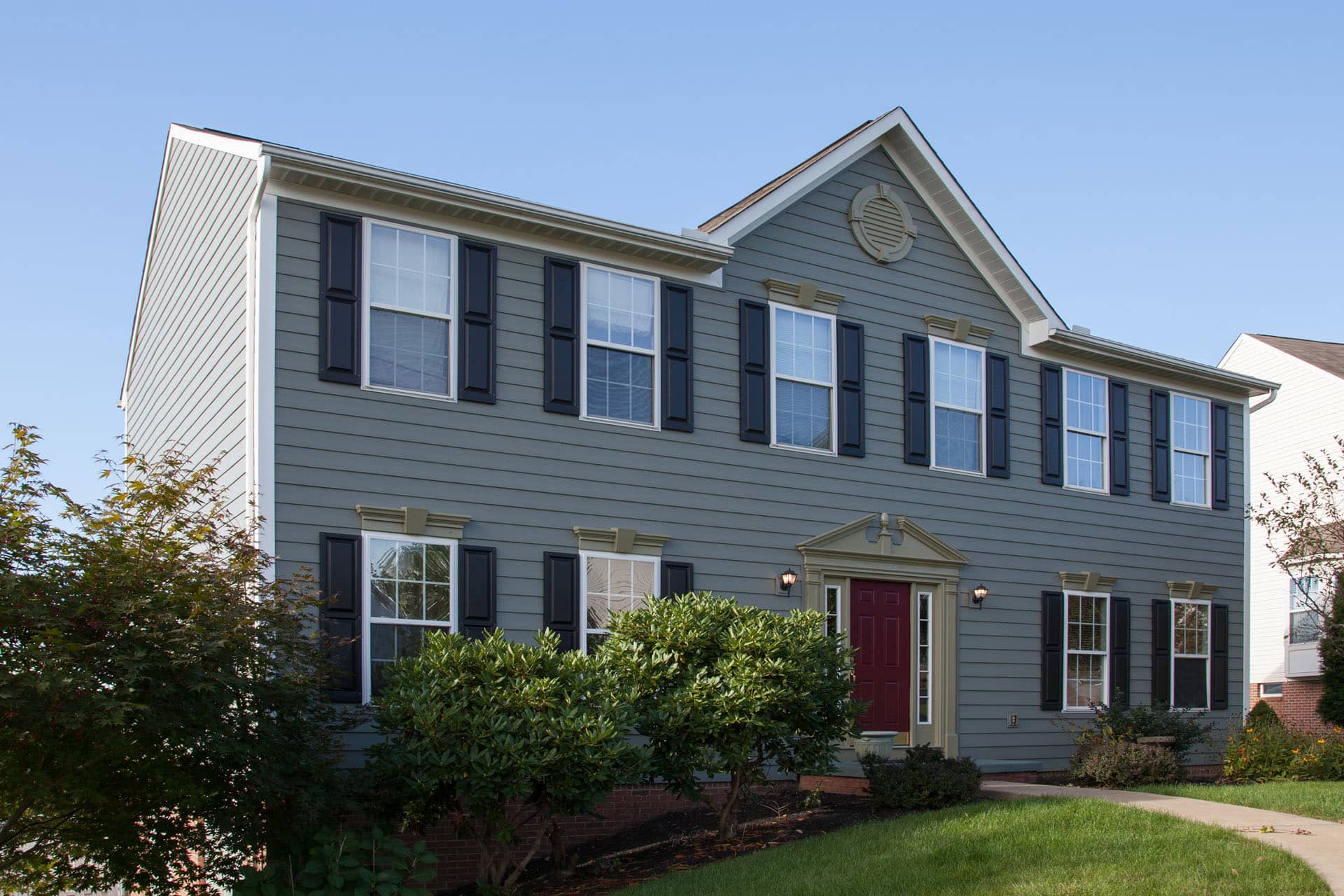 large colonial-style house with gray composite siding, large windows and red front door